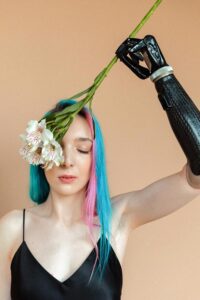 Junge Frau mit Armprothese streichelt sich mit einer Blume im Gesicht, ihre Augen sind dabei geschlossen